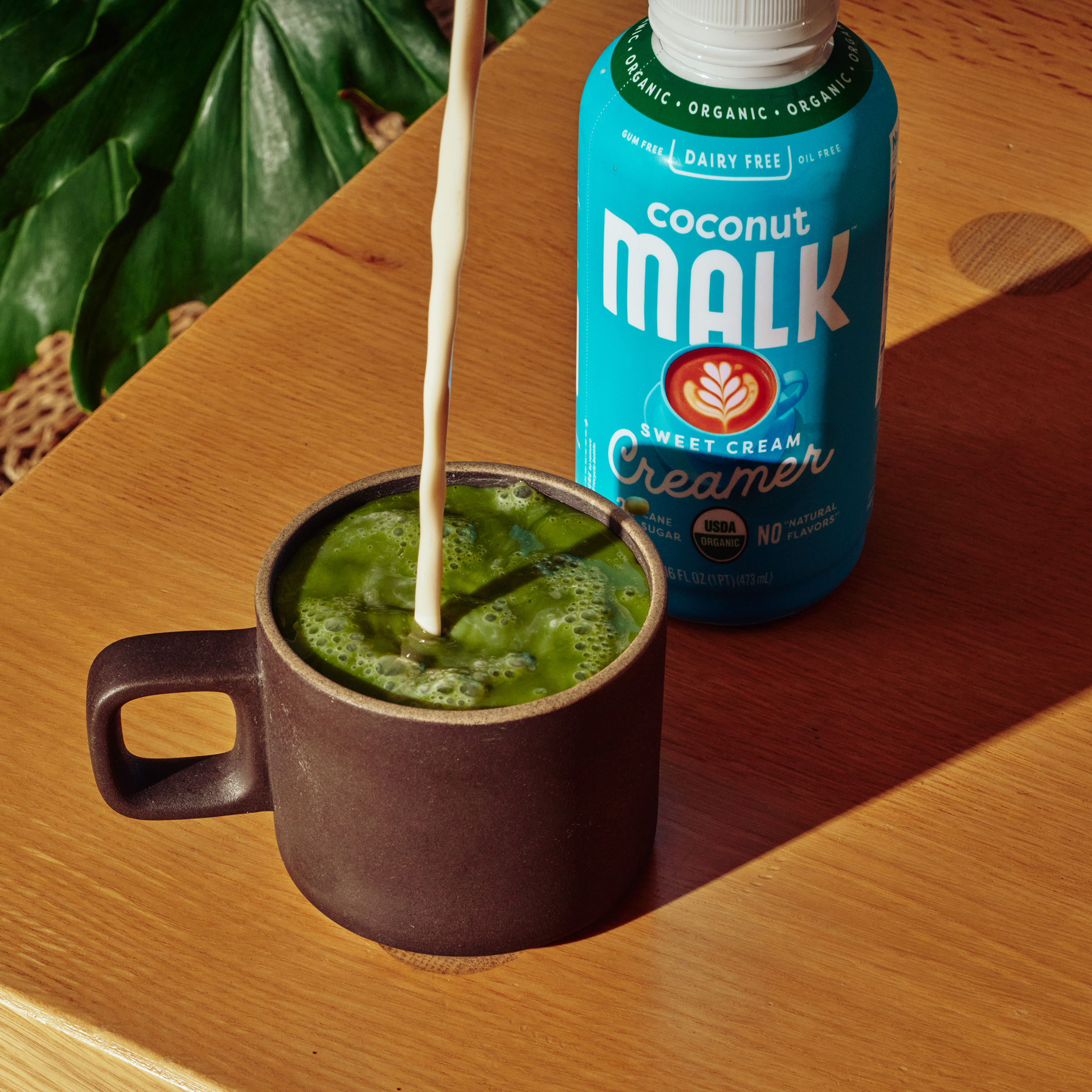 MALK Organic Non-Dairy Sweet Cream Coconut Milk Creamer next to a matcha latte with creamer being added to it