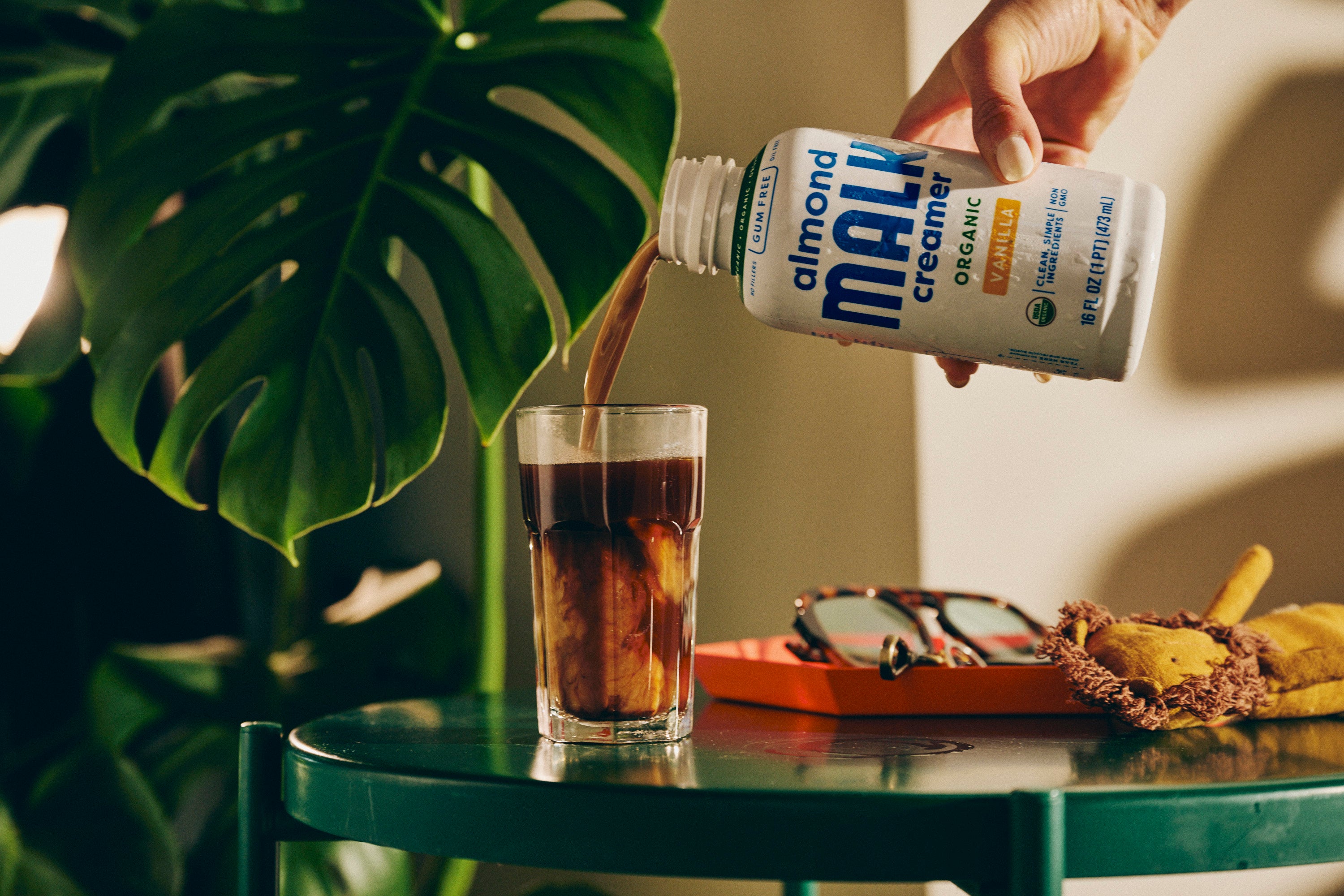 Bottle of almond creamer being poured over iced coffee in a beautiful modern setting