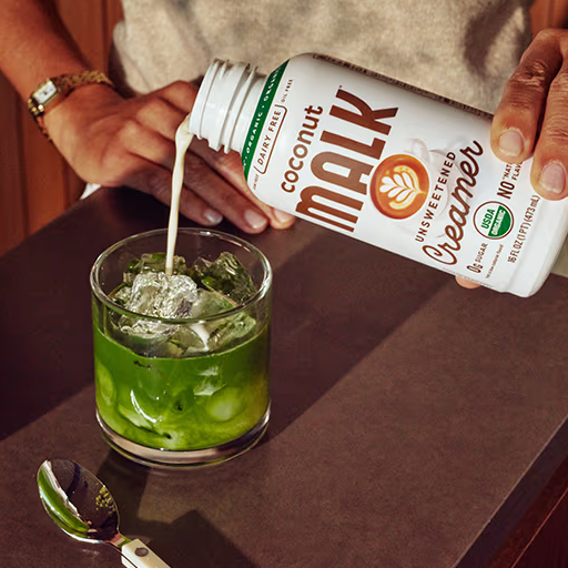 Bottle of MALK Unsweetened Coconut Coffee Creamer being poured into an iced green matcha drink