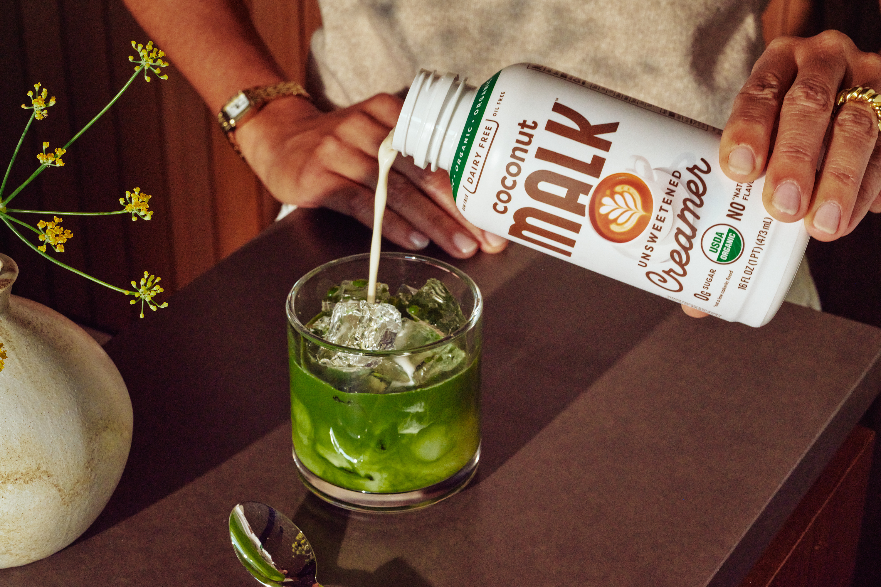 MALK Unsweetened Coconut Milk Creamer being poured into an iced matcha drink in a glass.